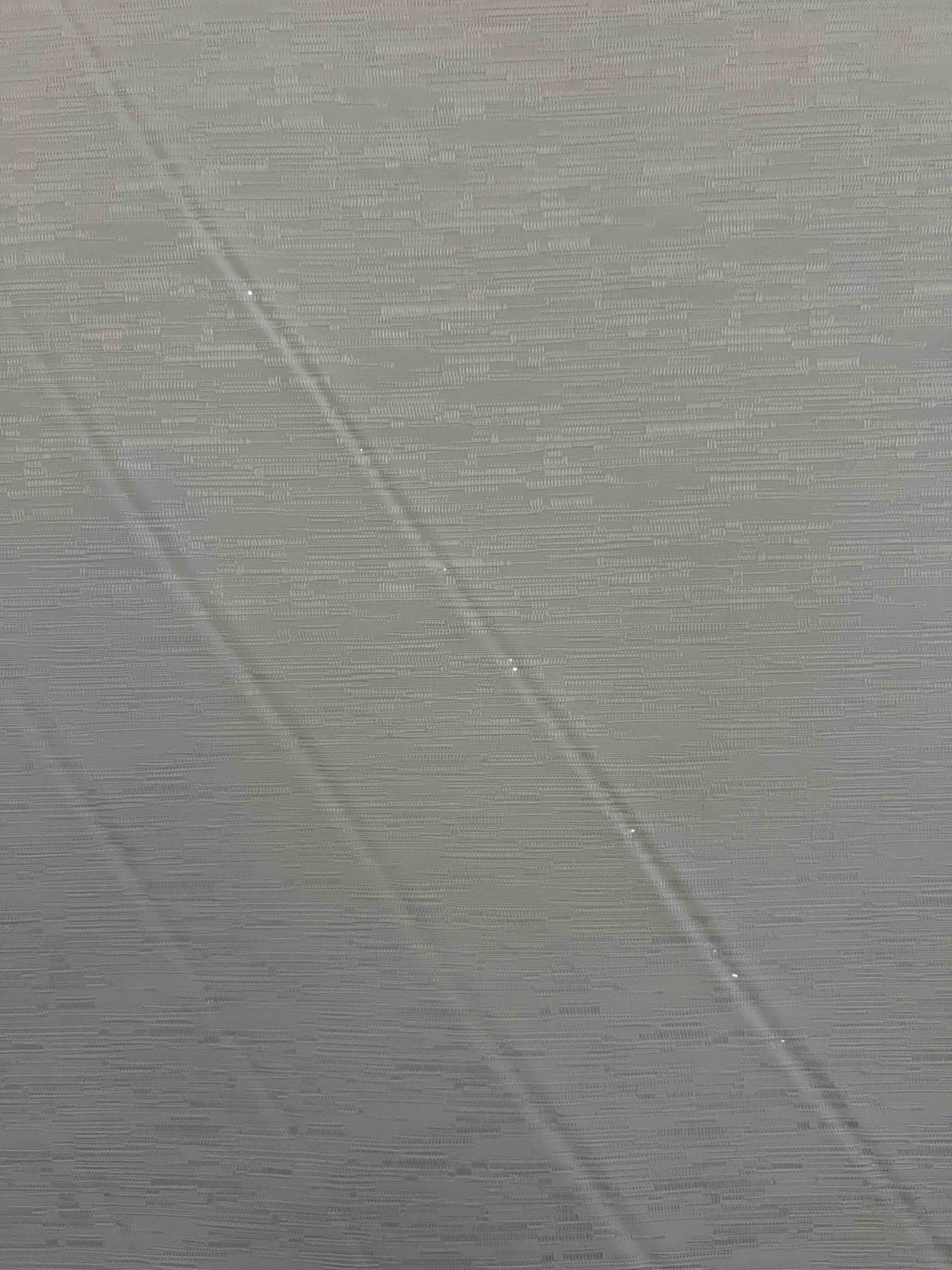 Close-up of fabric tearing and holes along V-shape wrinkles on an old motorized roller shade.