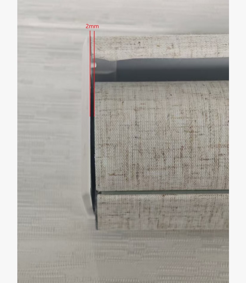 Close-up real-shot of a motorized roller shade showing a minimal 2mm light gap between the fabric edge and the end cap, demonstrating high-precision manufacturing.